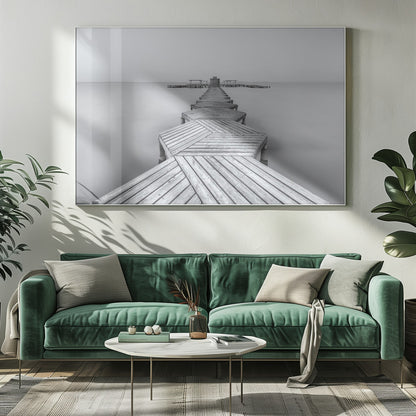 A framed, black and white photograph capturing a long wooden pier from a first-person perspective. The pier, constructed from a series of hexagonal platforms, stretches out into a calm, placid body of water that disappears into a foggy horizon, creating a serene and minimalist scene. Print