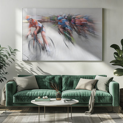 An action photograph of a professional cycling race captured with a prominent motion blur effect that conveys a strong sense of speed. A cyclist in an orange and black uniform is in the foreground, leaning into a turn, while a group of other riders in blue and multi-colored jerseys follows closely behind, their forms streaked and blurred. The entire scene is encased in a brushed silver frame. Poster