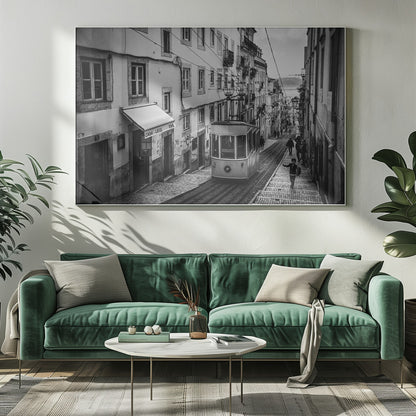 A black and white photograph of a vintage tram on a steep, narrow cobblestone street in an old European city. The street is lined with historic buildings and people are walking alongside the tracks. In the distance, a body of water is visible. Poster