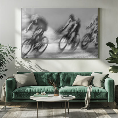 A dynamic black and white action photograph of three cyclists racing, captured with a slow shutter speed to create a dramatic motion blur effect. The riders and their bikes are blurred into streaks of light and shadow, conveying a powerful sense of speed and intensity. The image is presented within a silver-toned frame. Poster