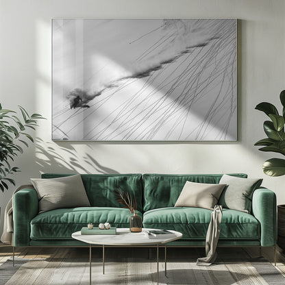 A dramatic black and white overhead photograph of a skier carving down a steep, powder-filled mountain slope, kicking up a huge plume of snow. Numerous ski tracks crisscross the pristine white snow, creating a pattern of dark lines. Poster