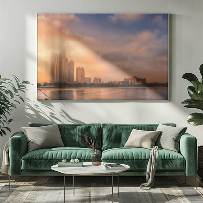 A framed photograph of the Abu Dhabi city skyline at sunset, featuring modern skyscrapers and the Emirates Palace hotel glowing in warm, orange light. The buildings are reflected in the calm water of the foreground, under a sky with soft orange and blue clouds. Poster