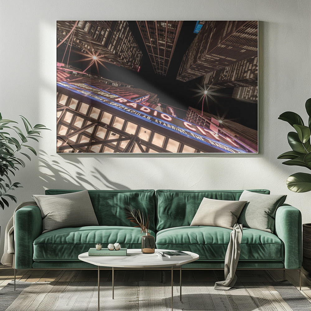 A dramatic low-angle shot looking up at the iconic Radio City Music Hall marquee at night, surrounded by towering, illuminated skyscrapers against a dark sky. Decor