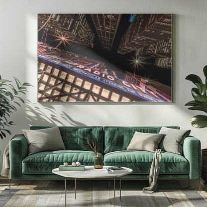 A dramatic low-angle shot looking up at the iconic Radio City Music Hall marquee at night, surrounded by towering, illuminated skyscrapers against a dark sky. Decor