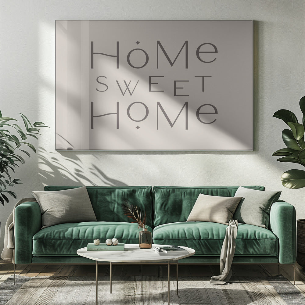 A minimalist wall art piece with the words 'Home Sweet Home' in a dark gray, stylized sans-serif font against a light beige background, all housed within a simple silver frame. Decor