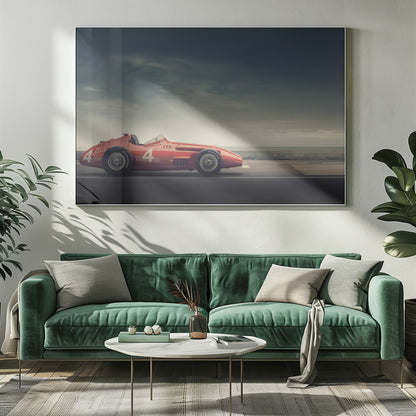 A side profile of a vintage red single-seater race car with the number 4 painted on it, parked on a seaside road under a dramatic, cloudy sky. The image has a muted, nostalgic color palette and is shown within a silver frame. Decor