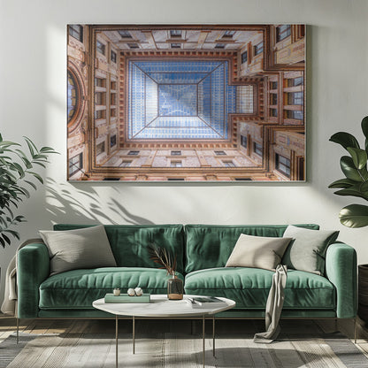 A worm's-eye view looking straight up from the center of an ornate, multi-story courtyard. The detailed walls create a symmetrical frame around a large glass skylight, which reflects a bright blue sky with fluffy white clouds. Print