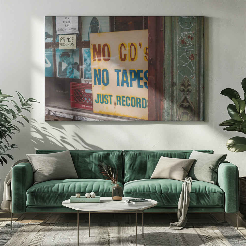 A weathered yellow sign in a record store window reads 'NO CD'S NO TAPES JUST RECORDS' in bold lettering. Behind the sign, vintage album covers and other posters are visible in the shop's display, next to a rustic green and brown door frame. Decor
