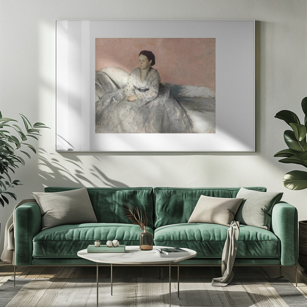 A framed impressionist painting of a woman with dark hair sitting on a bed against a dusty rose background. She wears a white, dotted blouse and a voluminous gray skirt, looking thoughtfully to her left. The painting is set in a silver frame with a white mat. Poster