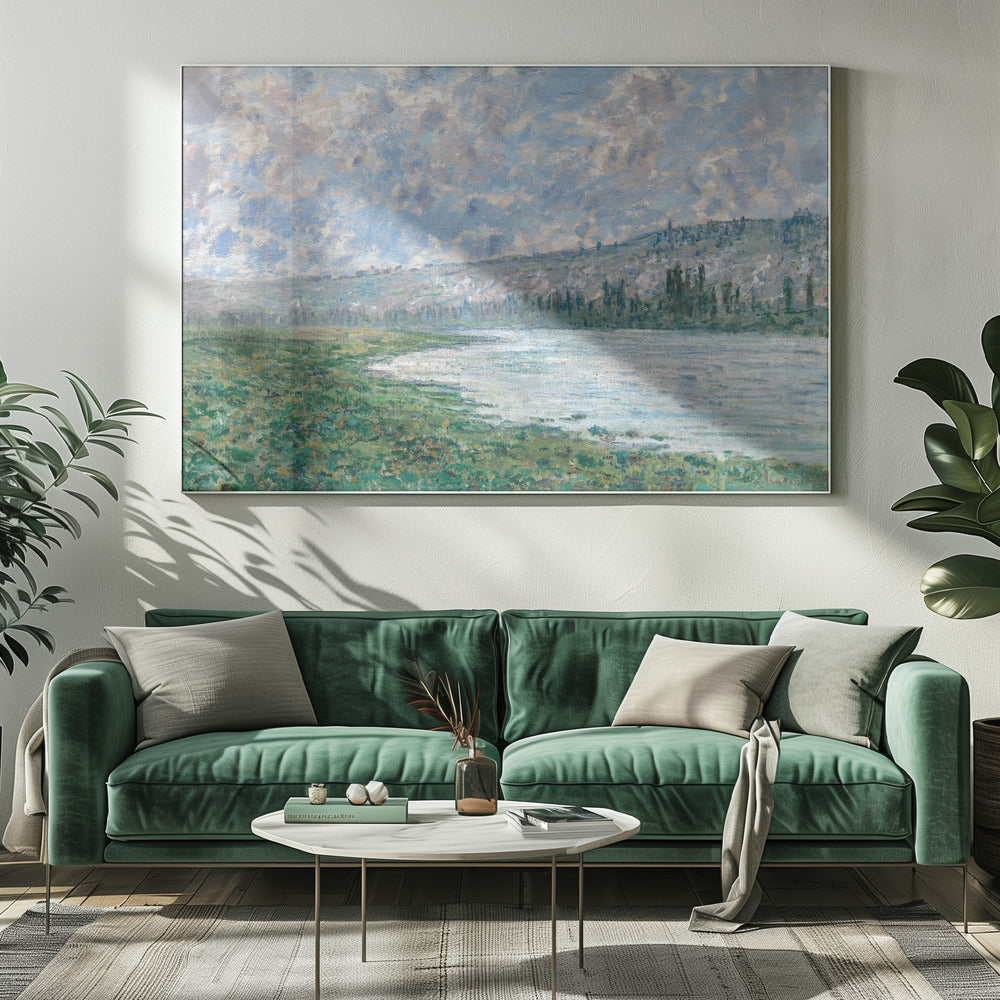 An Impressionist painting by Claude Monet, 'The Seine at Vétheuil', depicting a tranquil landscape. In the foreground, a lush green riverbank meets the calm, reflective water. A distant, soft-focus hillside rises under a vast sky filled with puffy white and grey clouds against a light blue background. The artwork is characterized by visible, textured brushstrokes and is displayed in a modern silver frame. Artwork