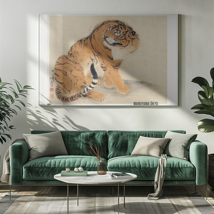 A vintage Japanese painting by Maruyama Ōkyo featuring a fluffy tiger sitting down and looking over its shoulder. The tiger has vibrant orange fur with black stripes and a white ruff. The background is a simple, textured beige paper with Japanese characters on the left. The artist's name is printed in the bottom right corner, and the entire piece is displayed in a silver frame. Print