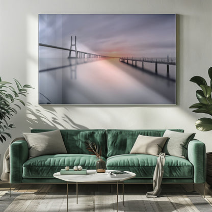 A serene long-exposure photograph of a modern cable-stayed bridge and a pier stretching over mirror-like water at sunset. The sky is filled with soft, streaky clouds in hues of pink and purple, reflected on the calm water's surface, all enclosed in a silver frame. Decor