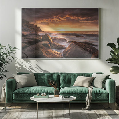 A framed photograph of a dramatic ocean sunset, with fiery orange clouds filling the sky. Large, dark rocks sit on the shore as long-exposure waves create a misty effect around them. Print