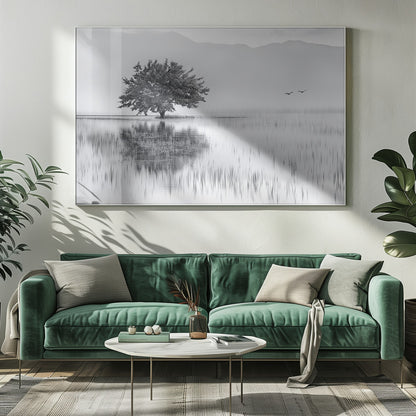 A serene black and white landscape photograph of a solitary tree standing in a calm lake, its reflection mirrored perfectly in the water. Hazy mountains are visible in the distance, and two birds fly across the pale sky, all enclosed within a silver frame. Print