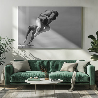 A framed, black and white photograph capturing a dynamic and romantic moment. A man is leaping off a diving board, carrying a woman who is wrapped around him in a passionate embrace, their faces close together. The background is a simple, plain gray, emphasizing their mid-air pose. Wall Art