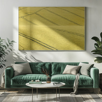 A framed photograph of a vast, rolling field of golden-yellow crops, with dark tractor tire tracks creating curving and diagonal lines across the hilly landscape. Decor