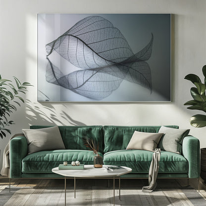 A close-up, macro photograph of a delicate skeleton leaf with intricate veins. The leaf is curled and resting on a reflective surface, creating a mirror image below it. The background is a soft, cool gradient from light blue to a darker muted teal. The image is presented within a brushed silver frame. Artwork