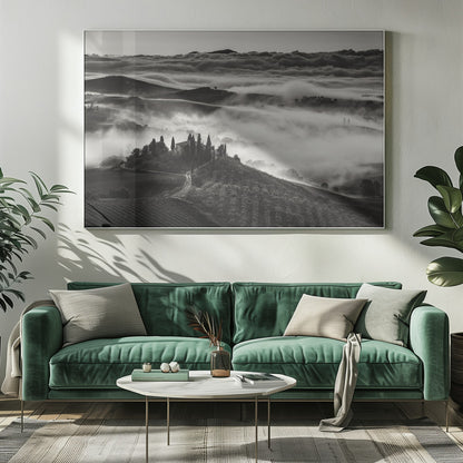 A framed, black and white photograph of a dramatic Tuscan landscape. A villa surrounded by cypress trees sits on a foreground hill, while thick fog blankets the rolling hills and valleys below. In the distance, a sea of clouds stretches towards a mountain range. Wall Art