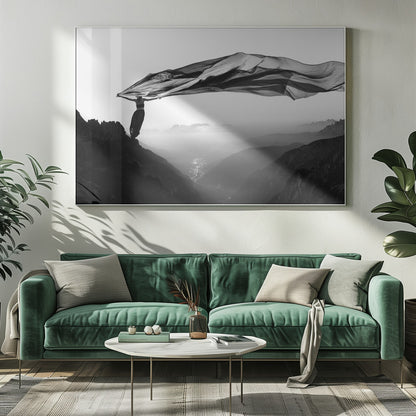 A dramatic black and white photograph of a woman standing on the edge of a mountain peak. She holds up a massive piece of dark, sheer fabric that billows in the wind, stretching across the sky. Below her, a vast, misty mountain range and a deep valley with city lights are visible. Wall Art