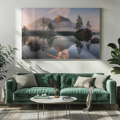 A serene mountain lake at sunrise or sunset, with a prominent peak illuminated by golden light. Small, rocky islands with pine trees dot the calm, clear water, which perfectly reflects the sky, trees, and mountains. A light mist hangs over the water and around the base of the mountains in the background. Decor