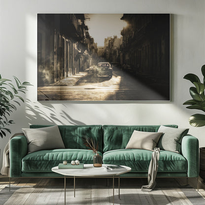 A sepia-toned, atmospheric photograph of a classic car driving down a narrow street in an old city. The sun hangs low, casting long shadows and illuminating smoke or dust in the golden air. Artwork