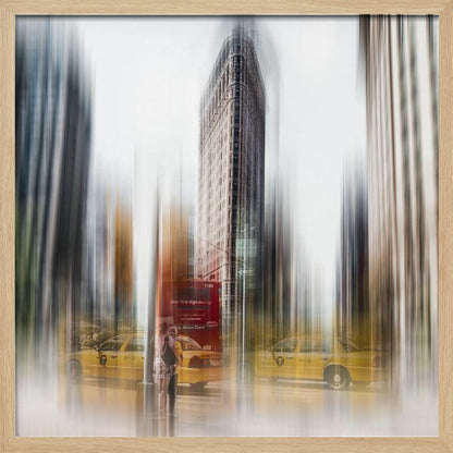 An artistic photograph of New York City's Flatiron Building in a light wood frame. The image has a strong vertical motion blur effect, creating streaks of yellow from taxi cabs and gray from the surrounding architecture, capturing the bustling energy of the city. Poster