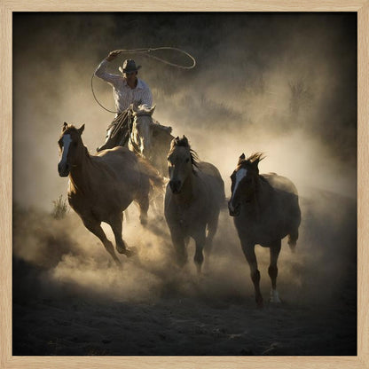 A dramatic, backlit photograph of a cowboy on horseback herding a small group of horses, kicking up a large cloud of dust as they gallop through a rustic landscape at sunrise or sunset. Poster