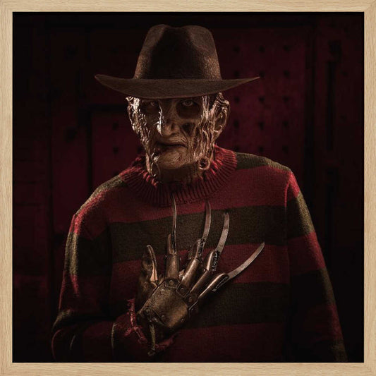 A framed portrait of the horror movie character Freddy Krueger, wearing his signature brown fedora, red and green striped sweater, and holding his bladed glove up to his chest in a menacing pose against a dark, shadowy background. Wall Art