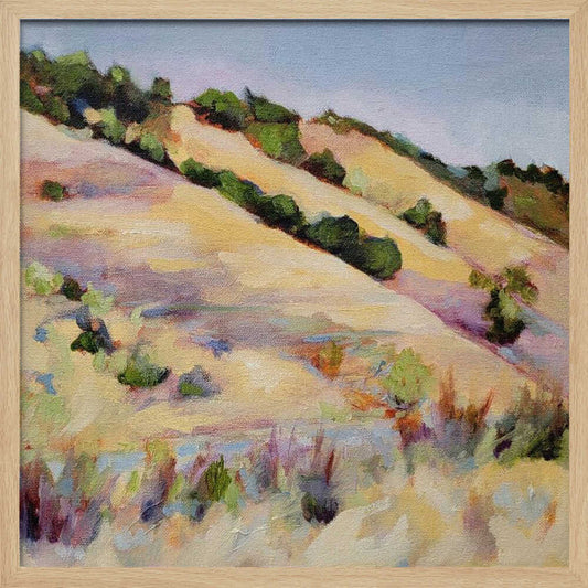 An impressionist oil painting of golden, rolling hills dotted with green shrubs under a pale blue sky, framed in light wood.