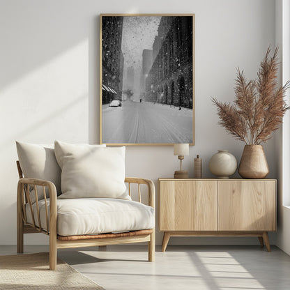 A grainy, black and white photograph captures a deserted city street during a heavy snowstorm. Tall buildings line the street, which is covered in a thick blanket of snow. A single car on the left is almost completely buried, and in the distance, a lone figure walks with an umbrella down the center of the empty road. Poster