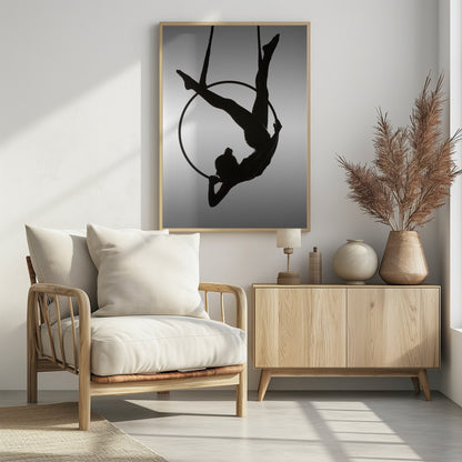 A black silhouette of a graceful female acrobat in an inverted pose on a suspended aerial hoop, set against a light grey background. Print