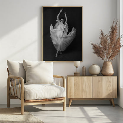 A framed, black and white photograph of a woman in a dramatic pose, wearing a voluminous white pleated dress. Her arms are raised above her head as the dress fans out around her in a sculptural, swirling motion. She looks directly at the camera against a solid dark gray background. Decor
