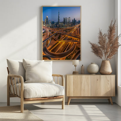 A long-exposure, aerial photograph of the Dubai skyline at dusk. The iconic Burj Khalifa stands tall in the center, surrounded by other illuminated skyscrapers against a deep blue twilight sky. In the foreground, a complex web of highways and overpasses glows with the orange and white light trails of moving traffic. Decor