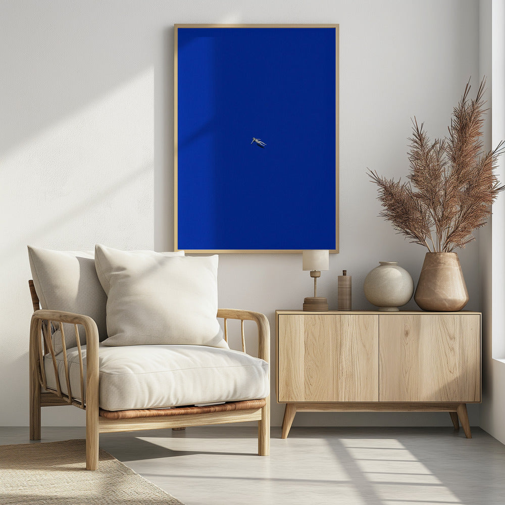 A minimalist and surreal artwork featuring a tiny, pale human figure floating peacefully in the center of an immense, solid, and vibrant blue void, all enclosed within a thin black frame. Wall Art