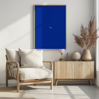 A minimalist and surreal artwork featuring a tiny, pale human figure floating peacefully in the center of an immense, solid, and vibrant blue void, all enclosed within a thin black frame. Wall Art