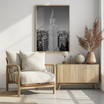 A high-angle, black and white photograph of the iconic Chrysler Building, its Art Deco spire prominently featured against the New York City skyline under a clear sky. Artwork