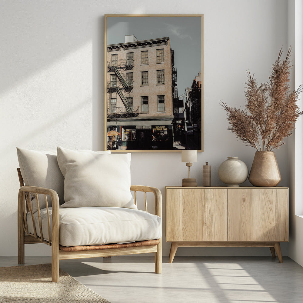 A low-angle, desaturated photograph of a classic brown brick building in a city, featuring multiple windows and a black metal fire escape zigzagging up the side. The sky is a pale, hazy blue, and the ground floor has dark storefronts. Decor