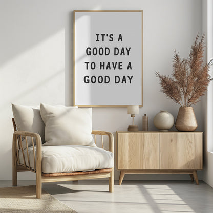 A framed black and white art print with the phrase 'IT'S A GOOD DAY TO HAVE A GOOD DAY' in a bold, dark gray, sans-serif font. Artwork