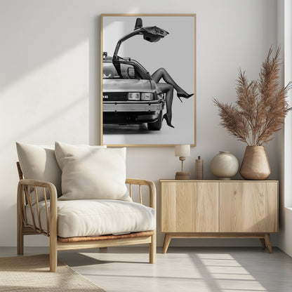 A black and white studio photograph of a DeLorean car with its gull-wing door open, featuring a woman's legs in black stockings and stilettos elegantly emerging from the passenger side. Decor