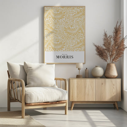 A framed exhibition-style poster of a William Morris design. The poster features an intricate, golden-yellow floral and leaf pattern on a white background. Below the pattern, the name 'WILLIAM MORRIS' is printed in black text. The entire artwork is presented in a simple black frame. Wall Art