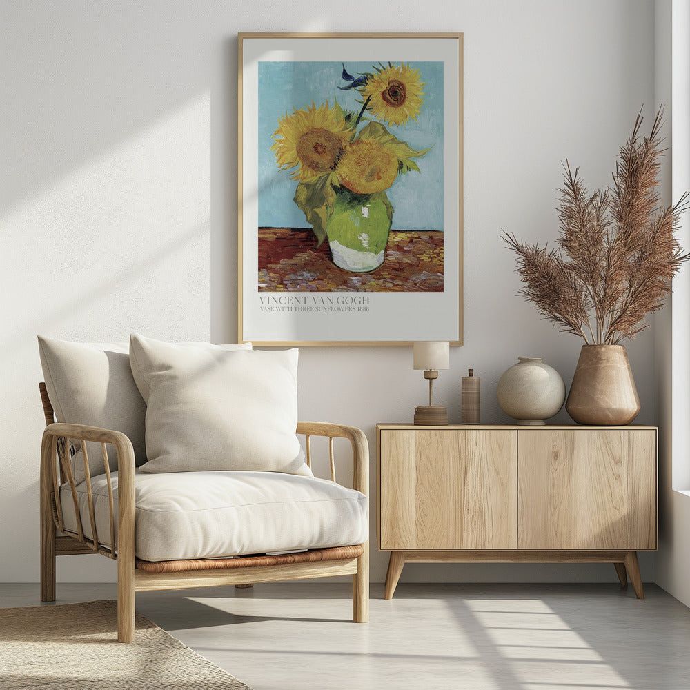 A framed art print of Vincent van Gogh's painting 'Vase with Three Sunflowers' from 1888. The artwork features three large, vibrant yellow sunflowers in a green vase set against a textured light blue background. The painting is in the post-impressionist style with thick, visible brushstrokes. The print has a white border with text at the bottom identifying the artist and title. Print