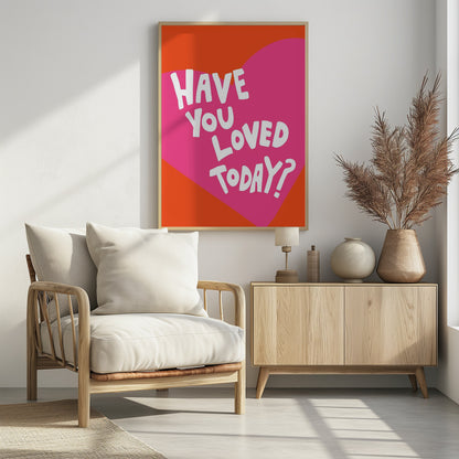 A framed art print with the text 'Have you loved today?' in a playful white font. The text is centered on a large pink heart which is set against a vibrant orange background. Artwork