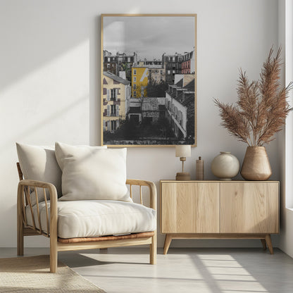 A framed, vertical photograph with selective color, showing a dense cluster of Parisian-style buildings under an overcast sky. Most of the image is in black and white, but one building is a vibrant yellow with a large white 'A' painted on it, creating a striking focal point. Wall Art