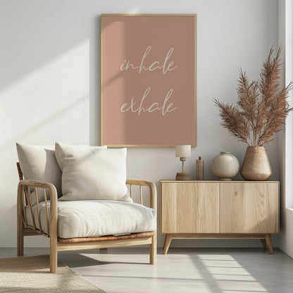 A minimalist framed poster featuring the words 'inhale' and 'exhale' in a flowing white script font, stacked vertically against a solid dusty pink background. Poster