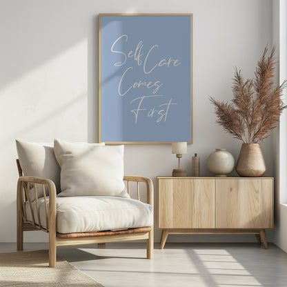 A framed poster featuring the phrase 'Self Care Comes First' in an elegant, off-white cursive font against a solid light blue background. The artwork is enclosed in a simple black frame. Decor