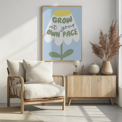 A motivational art print featuring a stylized white flower with a yellow center and green stem against a light blue background. The phrase 'GROW at your OWN PACE' is written in green, hand-drawn lettering across the flower's petals. Artwork