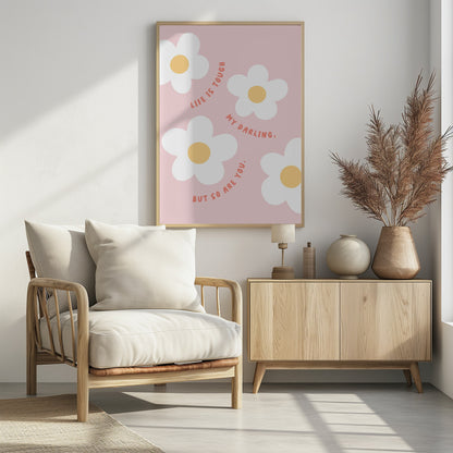 A motivational art print with a light pink background featuring four simple, stylized white daisies with yellow centers. The quote 'Life is tough my darling, but so are you.' is written in a playful, reddish-orange handwritten font that curves around the flowers. Artwork