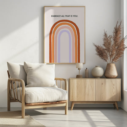 A framed art print with an inspirational quote. On a cream background, the black text reads 'EMBRACE ALL THAT IS YOU.' Below the text is a large, stylized U-shaped rainbow with thick, painted bands of terracotta, orange, pink, and lavender. Print