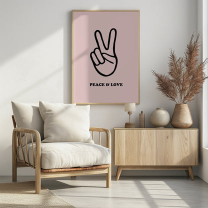 A minimalist art print with a light pink background featuring a bold black outline of a hand making a peace sign. Below the hand, the words 'PEACE & LOVE' are printed in a black serif font. The print is enclosed in a simple black frame. Print