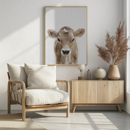 A close-up portrait of a light brown baby cow looking directly at the camera against a stark white background, enclosed in a simple black frame. Artwork
